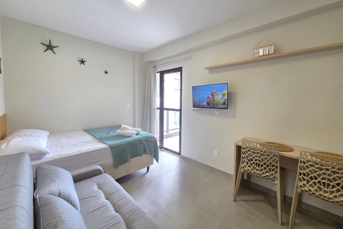 A hotel room with a bed, a sofa, a TV, and a window with curtains.