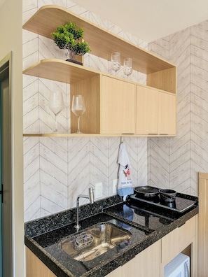Una cucina con zoccolo paraschizzi a motivi a spina di pesce, mobili in legno, un piano di lavoro in granito nero, un lavello in acciaio inossidabile e una piccola pianta in vaso su uno scaffale.