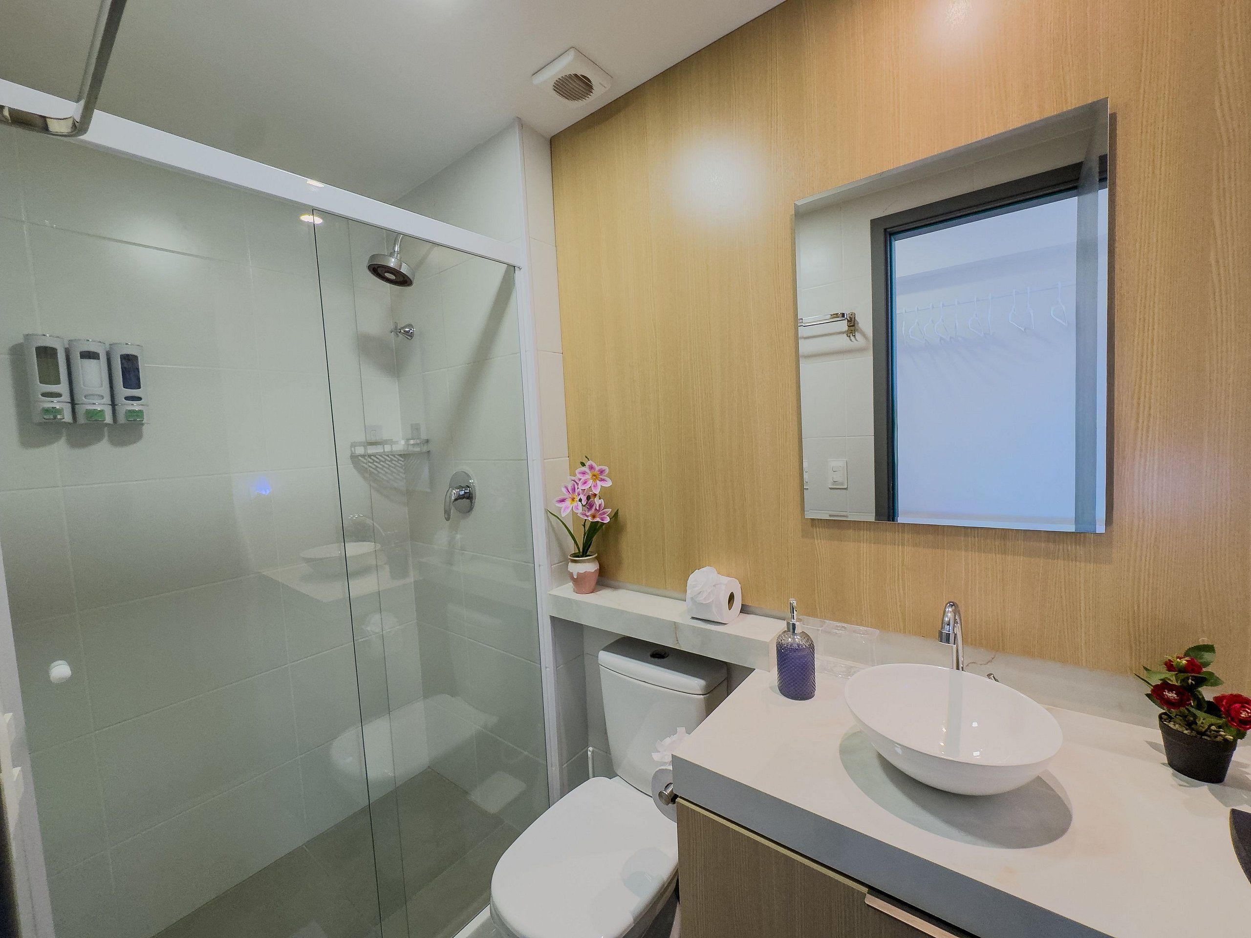 A modern bathroom with a glass-enclosed shower, a white sink with a bowl, a toilet, and a mirror above the sink.
