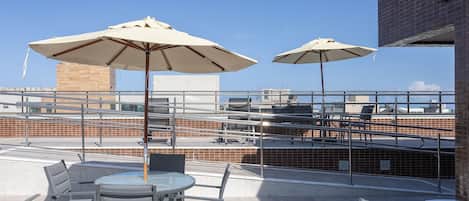 An outdoor seating area with tables and chairs, two umbrellas, and a view of the cityscape.