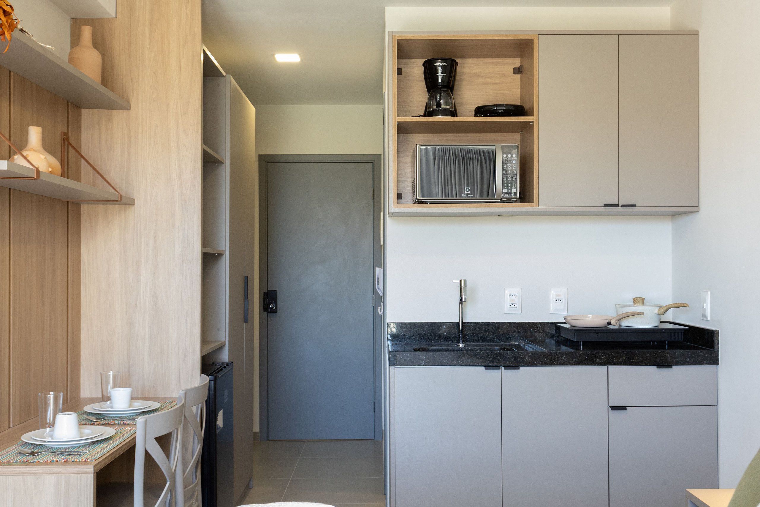 A modern kitchen with a black countertop, stainless steel appliances, and wooden shelves.