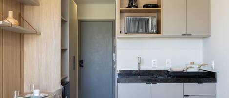 A modern kitchen with a black countertop, stainless steel appliances, and wooden shelves.