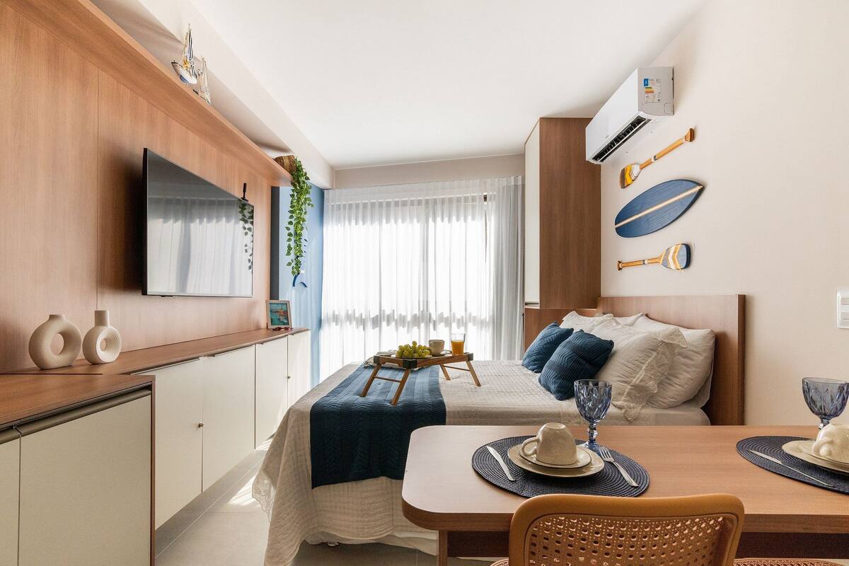 A hotel room with a bed, bedside table, TV, and a dining area with a table and chairs.