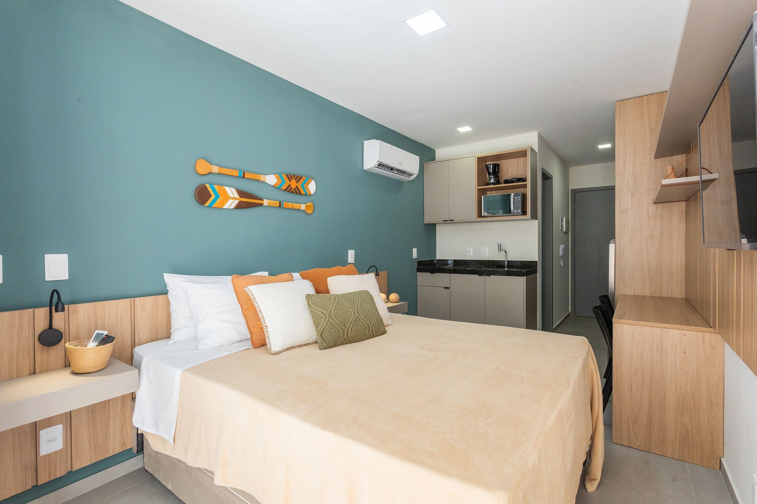 A modern hotel room with a bed, a small kitchen area, and a TV.