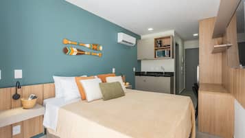 A modern hotel room with a bed, a small kitchen area, and a TV.