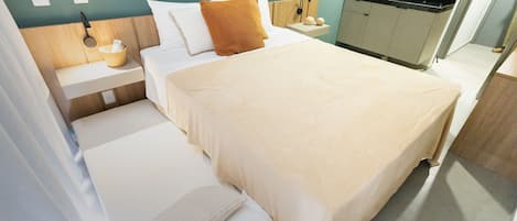 A hotel room with a bed, a bedside table, a small kitchen area, and a wall-mounted radio.