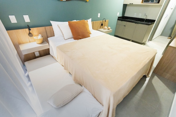 Una camera d'albergo con un letto, un comodino, una piccola cucina e una radio fissata alla parete.