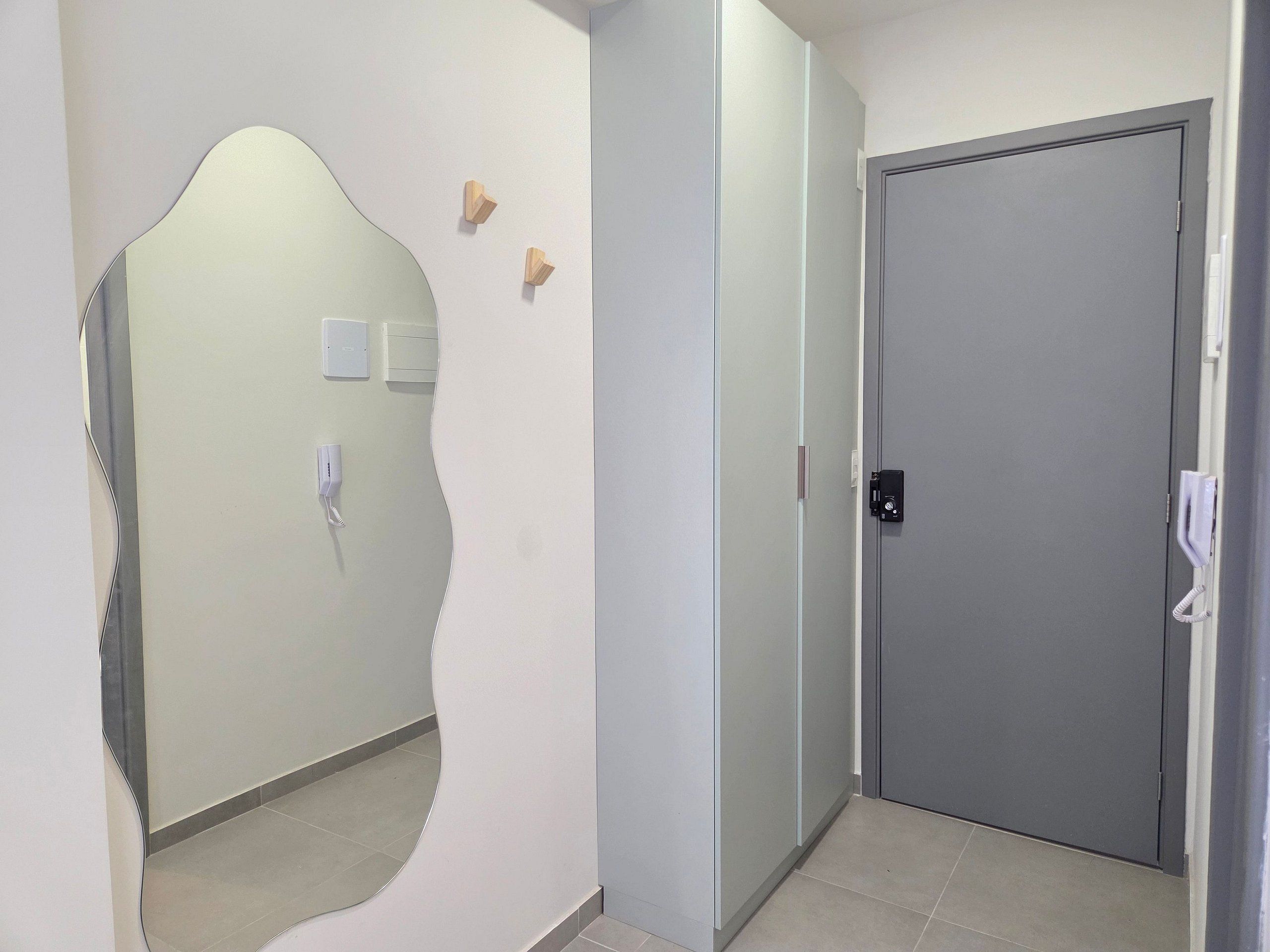 A hallway with a mirror, a door, and a phone on the wall.