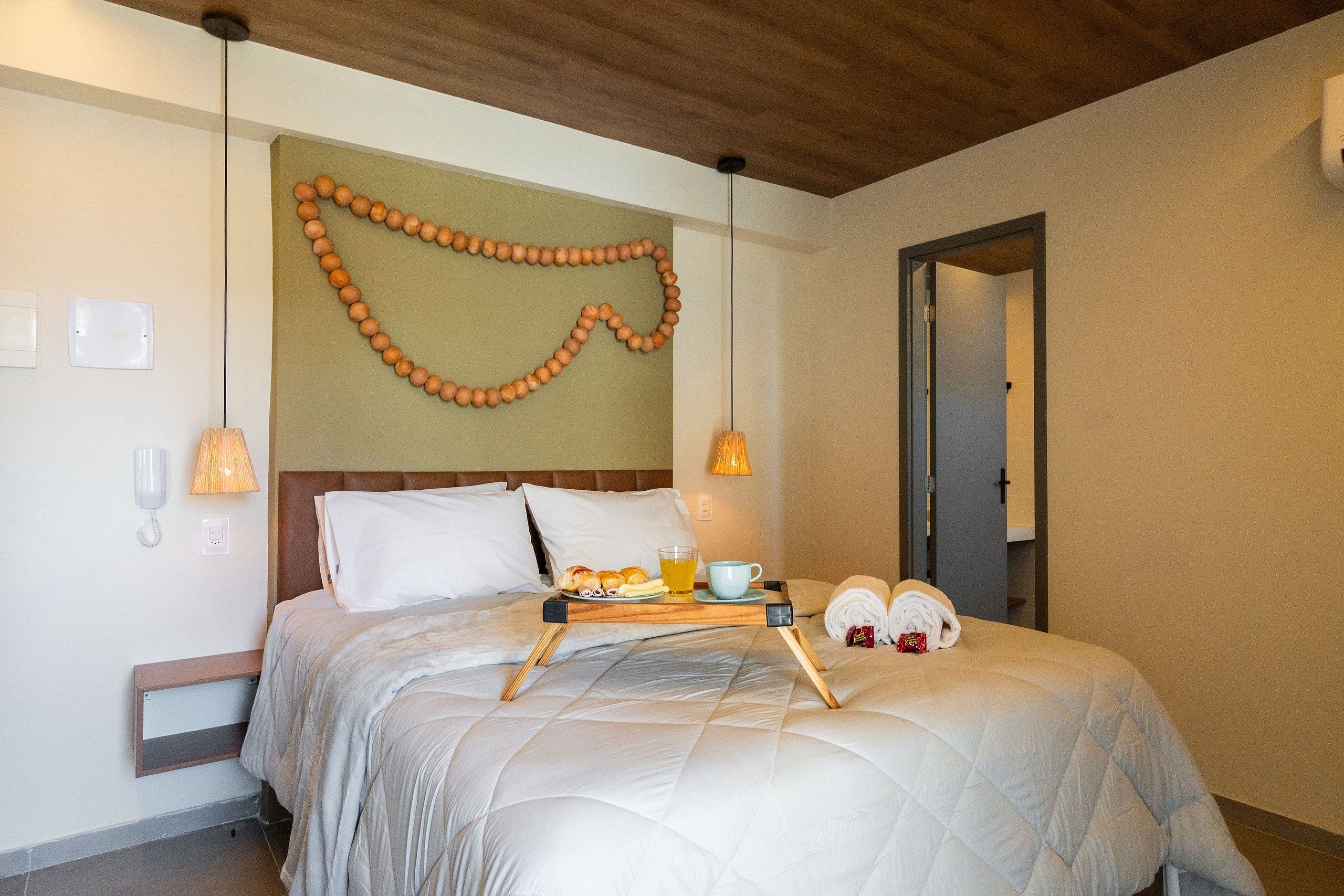 A hotel room with a bed, bedside lamps, a tray with breakfast items, and a wall decoration.