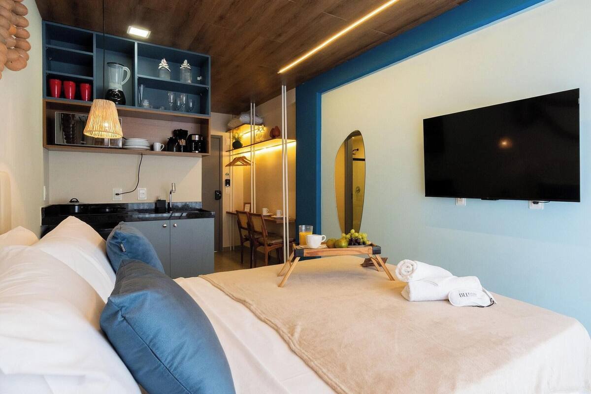 A hotel room with a bed, a desk, a mirror, and a TV.