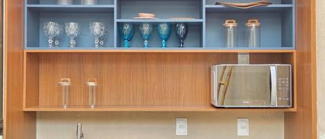 A kitchen with a microwave, a sink, and shelves with glassware and jars.
