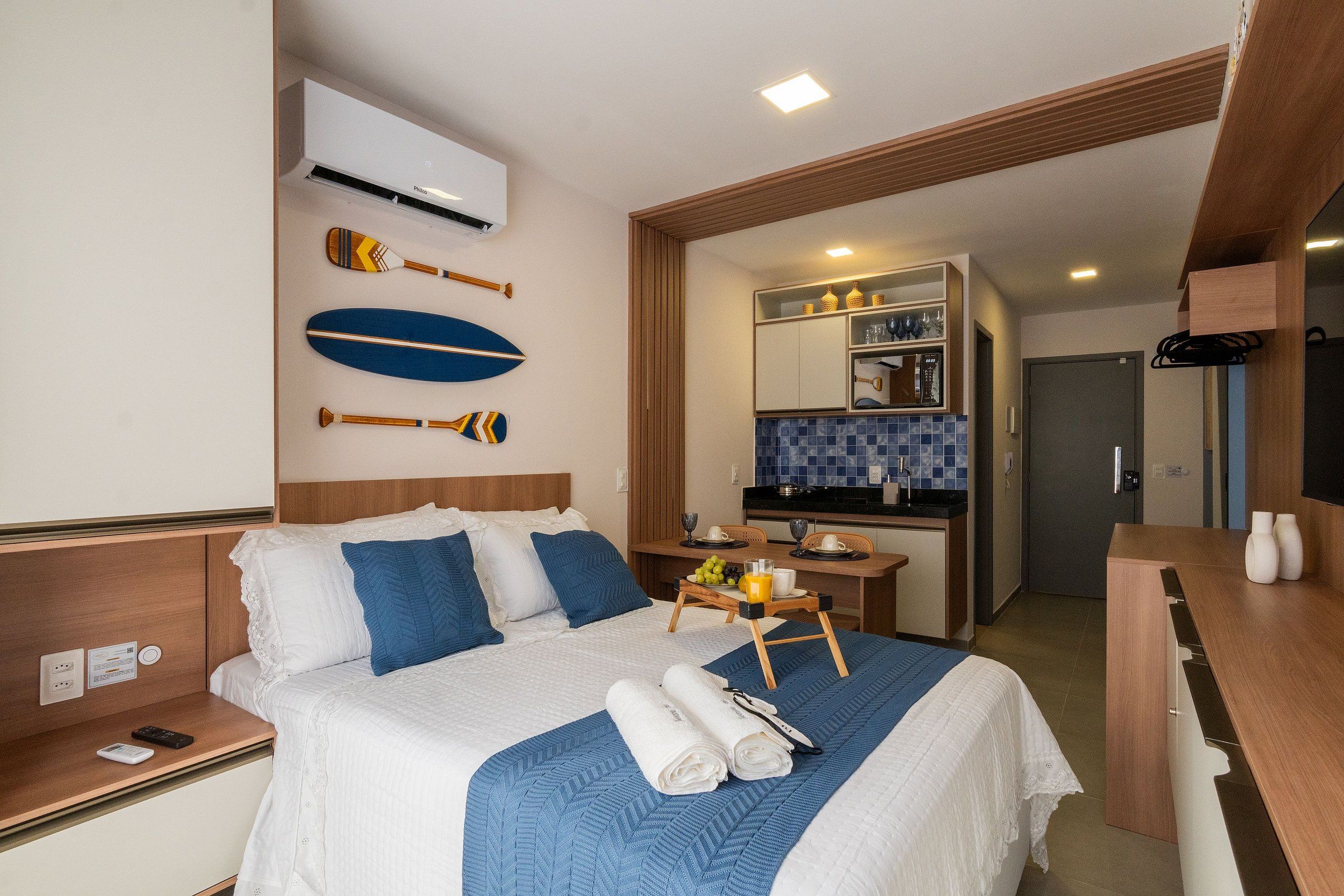 Ein Hotelzimmer mit Bett, Schreibtisch mit Obstschale und Tasse, einer Küchenzeile und einem Badezimmer.