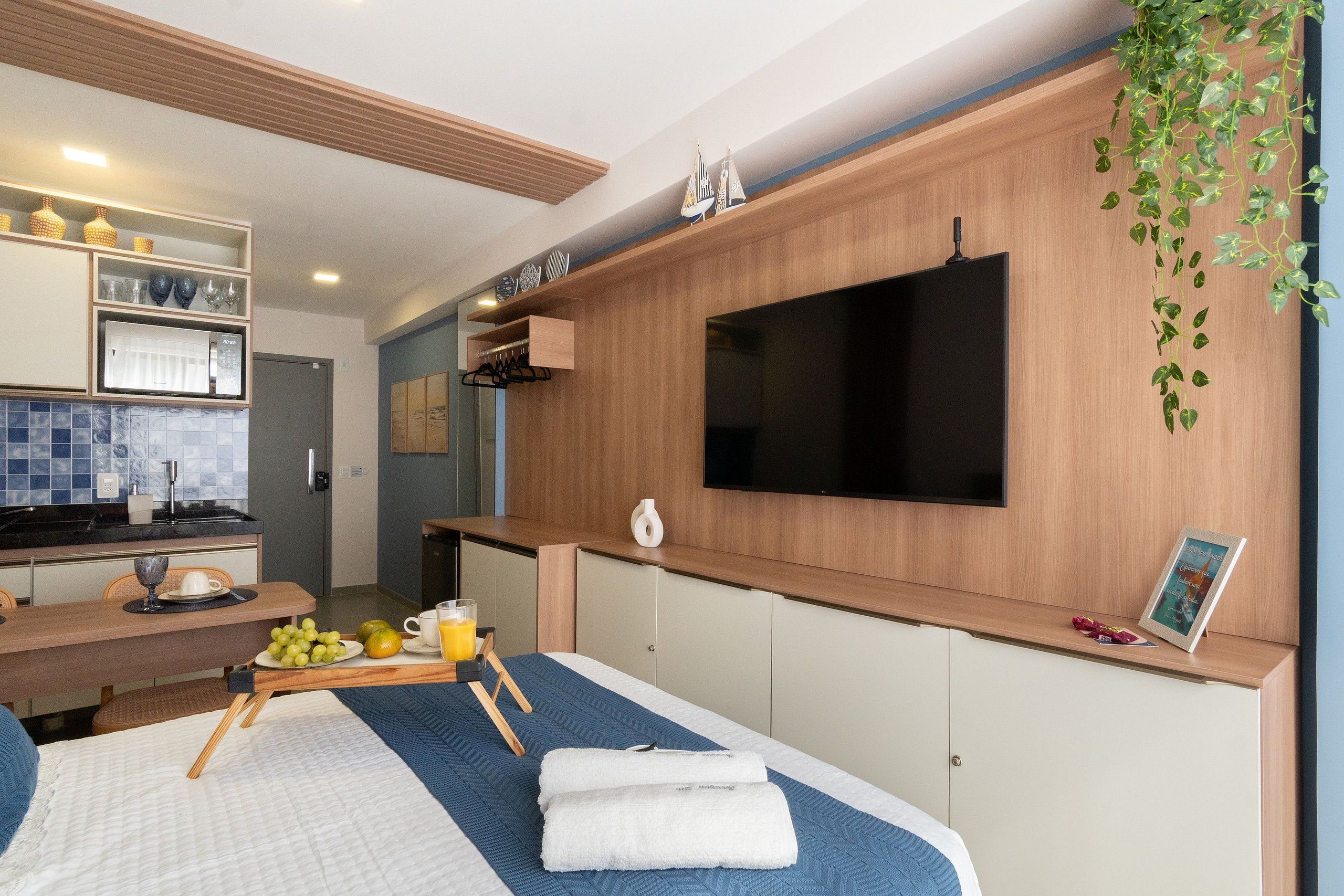 Una habitación de hotel moderna con una cama, un televisor montado en la pared, una pequeña cocina y una mesa de comedor.