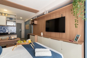 Ein modernes Hotelzimmer mit Bett, Wand-Fernseher, kleiner Küchenzeile und Esstisch.
