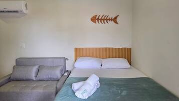 Una stanza con un letto, un divano grigio, un condizionatore d'aria a muro e una decorazione a forma di pesce.