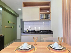 A dining area with a table set for two, a microwave, and a cabinet above the counter. - SEASON Smart Flats by BLU stay (Ipojuca)