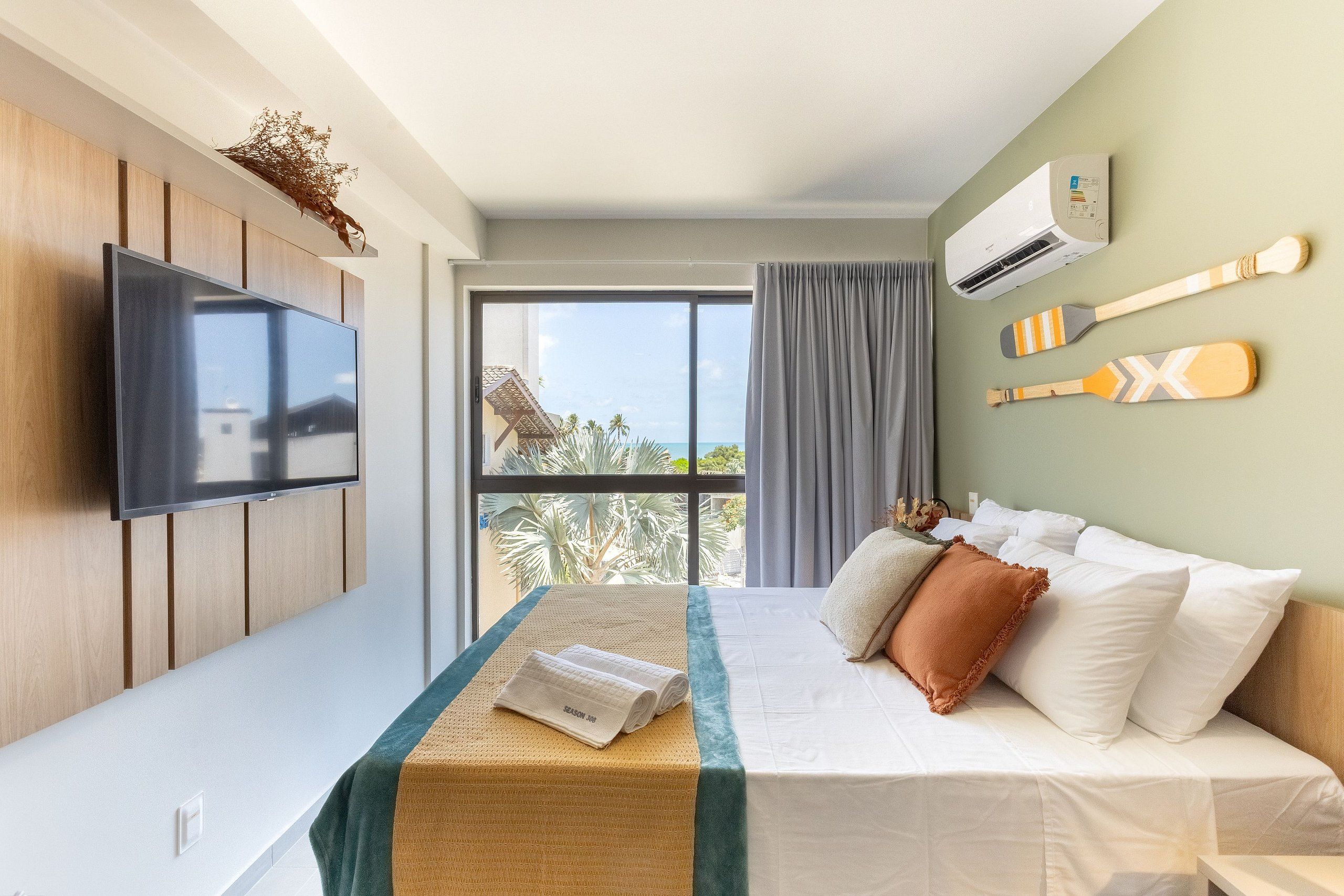 Ein Hotelzimmer mit Bett, Flachbildfernseher, Klimaanlage und Blick auf Palmen.