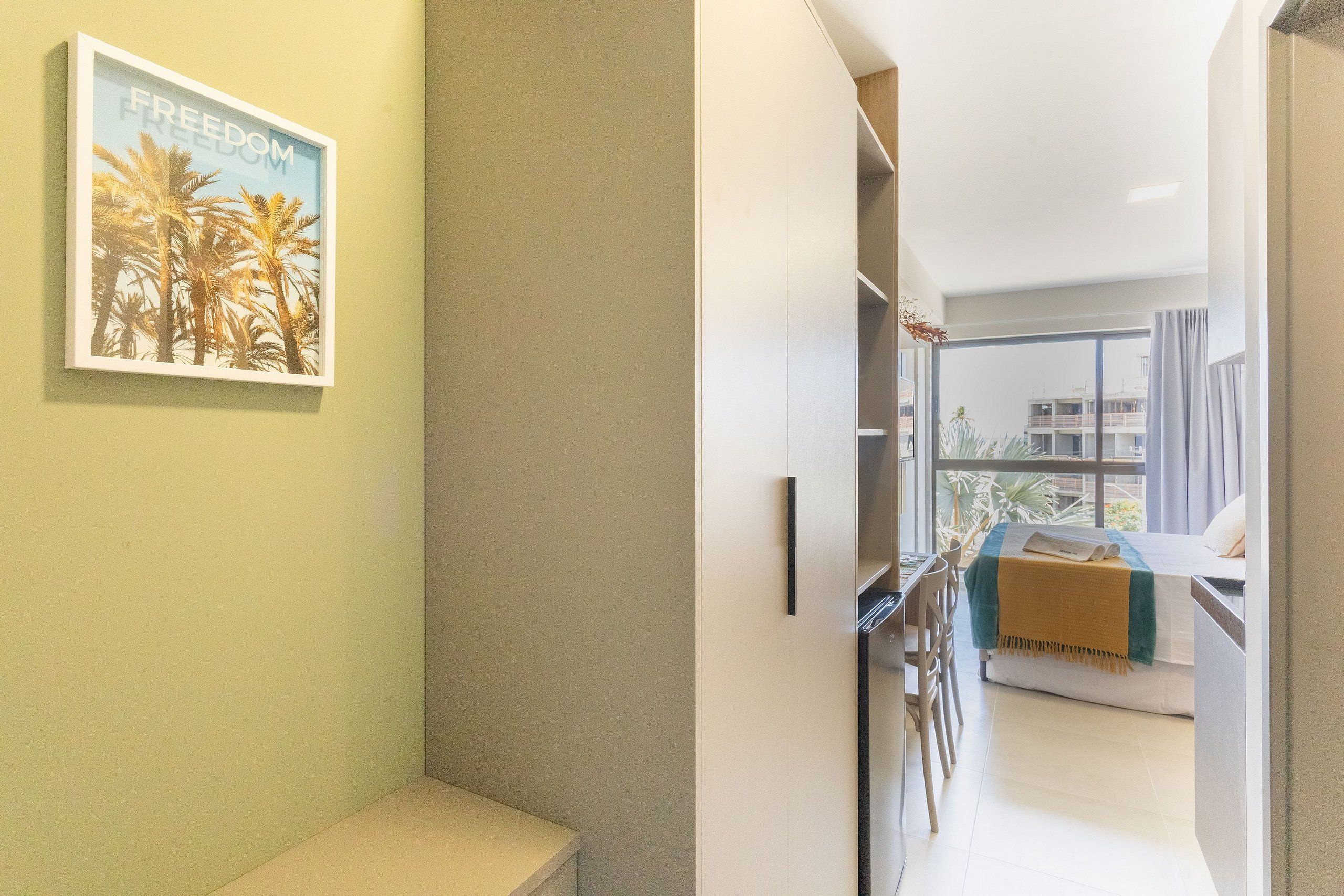 A hotel room with a bed, a desk, a chair, and a view of the outside.