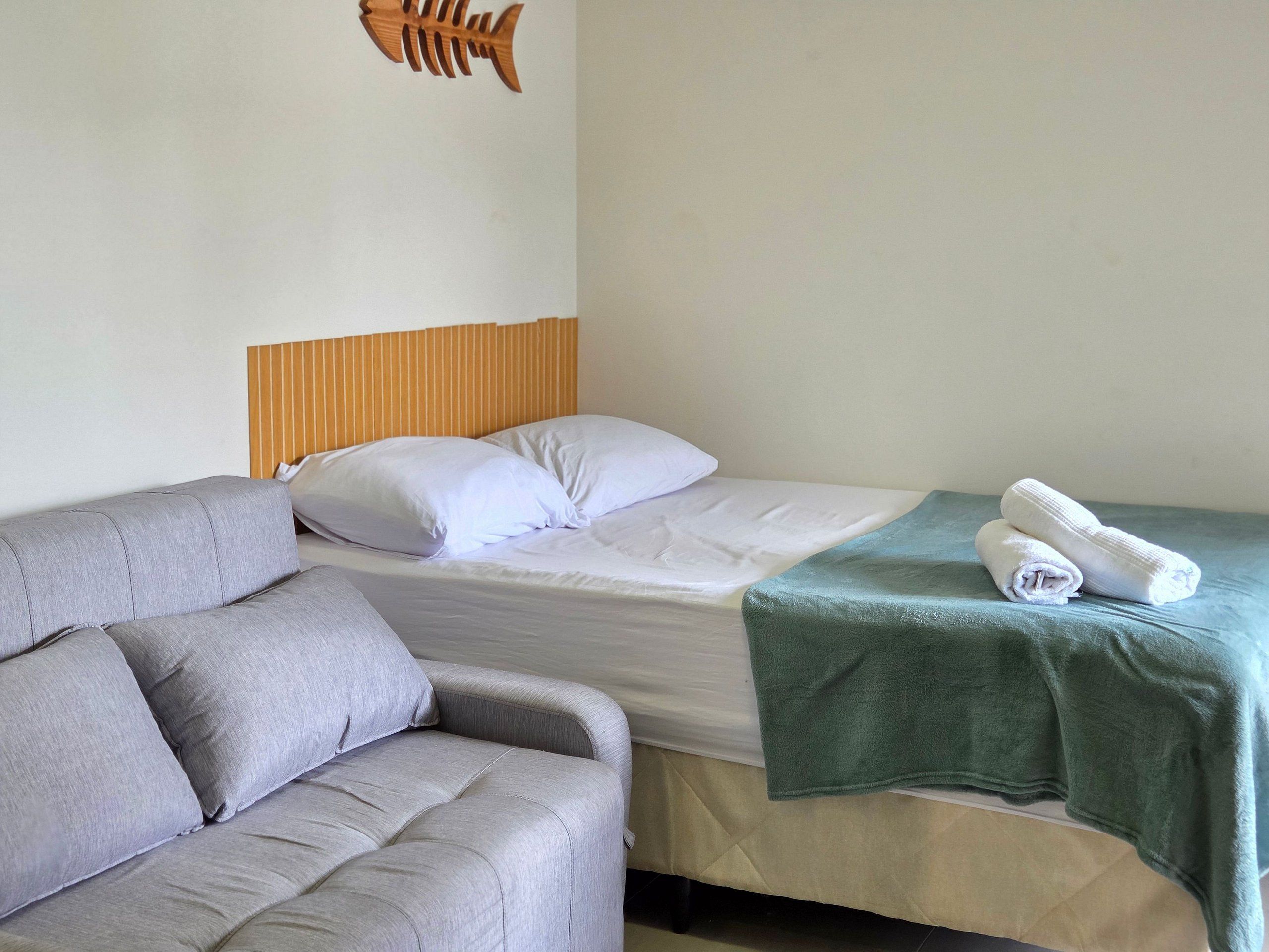 A single bed with white bedding, a green towel, and a wooden fish decoration on the wall.