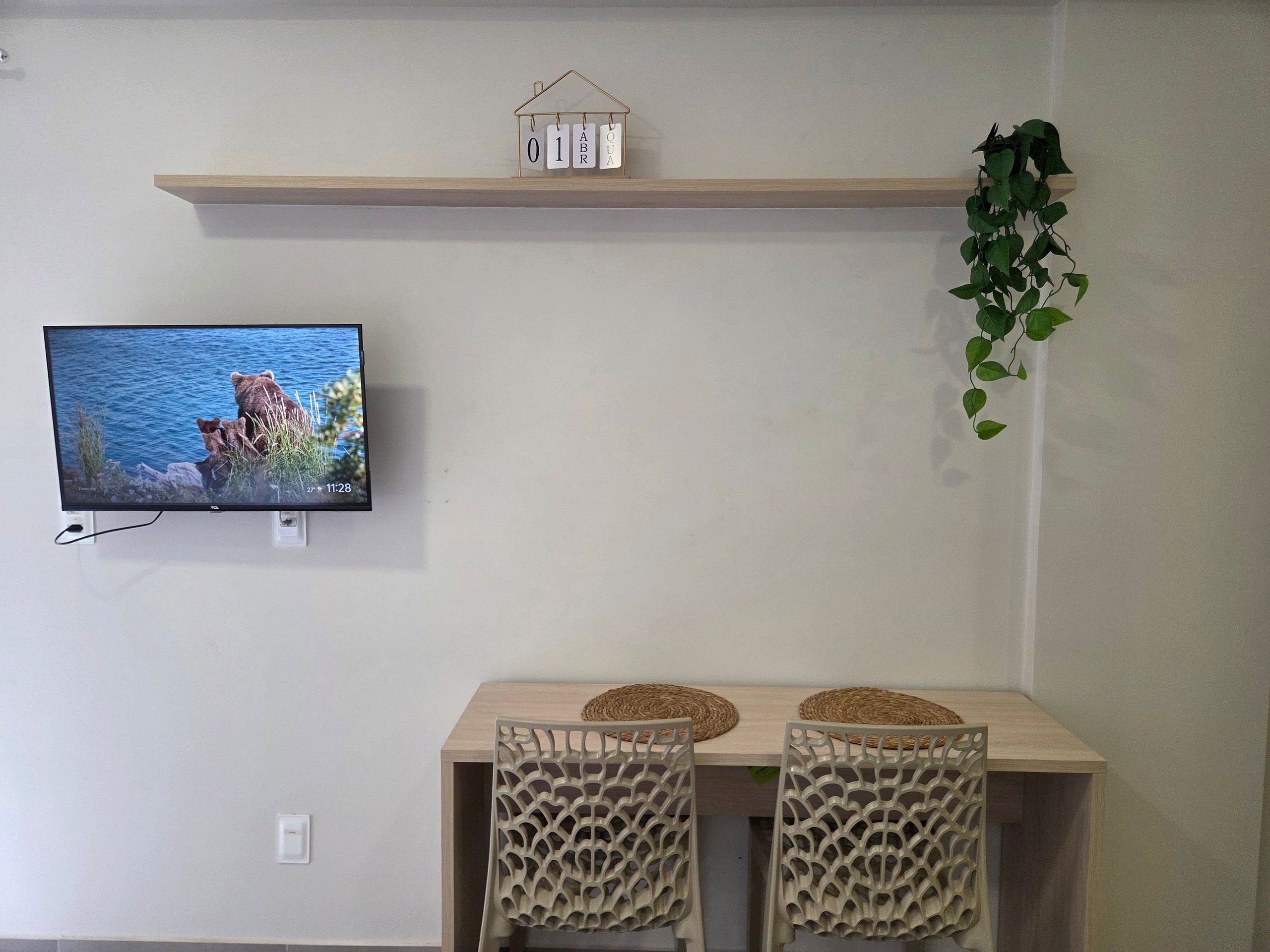 A room with a TV displaying a bear and water, a wooden shelf with a house-shaped calendar, and a plant.