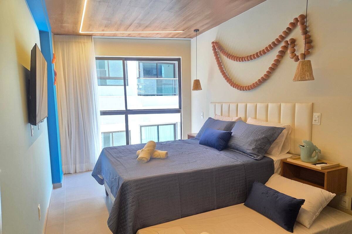 A hotel room with a large bed, a bedside table, a wall-mounted TV, and a window with curtains.