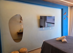 A room with a bed, a TV mounted on the wall, a mirror, and a small shelf with items. - SEASON Smart Flats by BLU stay (Ipojuca)