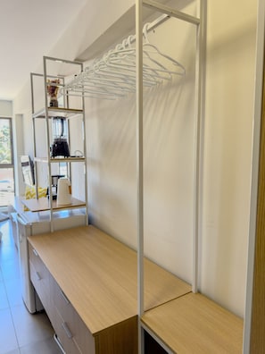 A modern, minimalistic room with a wooden desk, a built-in shelf unit, and a hanging clothes rack. - SEASON Smart Flats by BLU stay (Ipojuca)