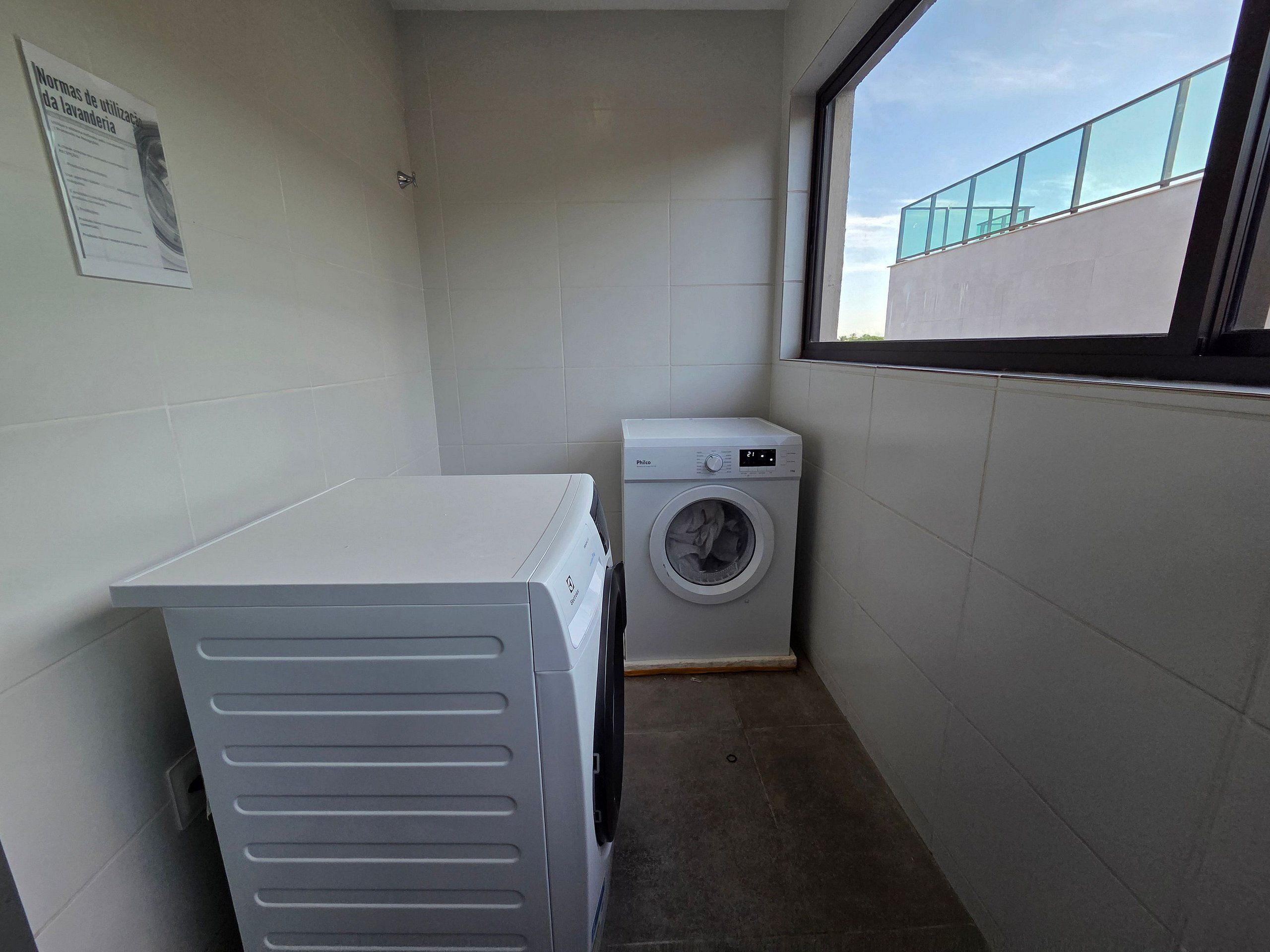 A laundry room with a washing machine, a drying rack, and a window with a view of a building.