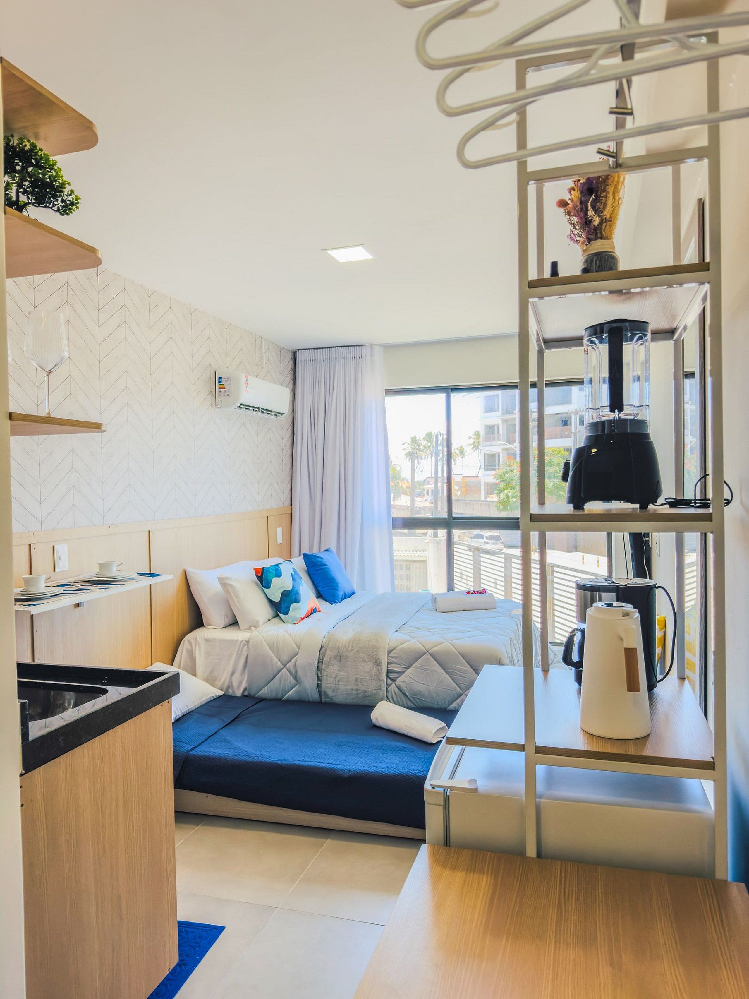 A compact hotel room with a bed, a kitchenette, a coffee maker, and a window with a view.