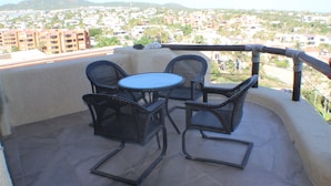 Un balcon avec une table et des chaises, donnant sur un quartier résidentiel avec des immeubles et des collines.
