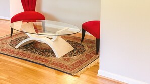 A modern living room with a glass coffee table, red chairs, a patterned rug, and a large mirror on the wall. - Spacious 4BR Rockville Yard, BBQ & Free Parking (Rockville)