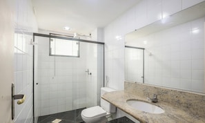 A bathroom with a glass shower enclosure, a white toilet, a granite countertop sink, and a large mirror.