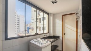 A compact bathroom with a large window, a washing machine, a sink, and a door.