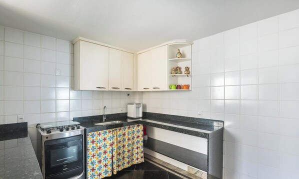 Una cocina con armarios blancos, estufa, fregadero y un estante con adornos.