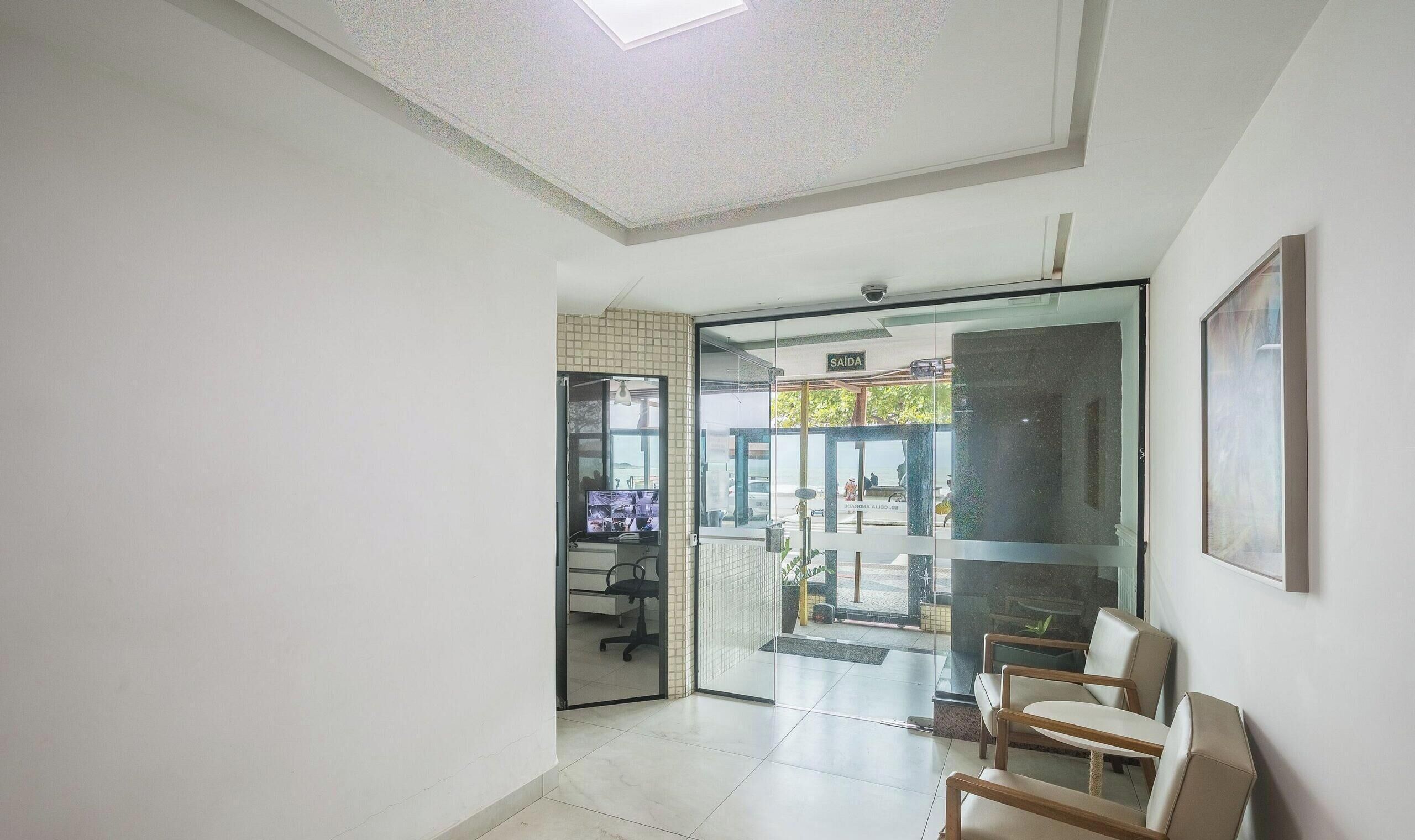 Um corredor com porta de vidro que dá para uma área de estar com cadeiras e uma televisão.