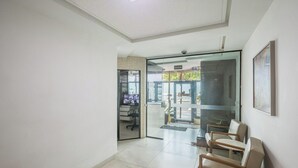 A hallway with a glass door leading to a seating area with chairs and a television.