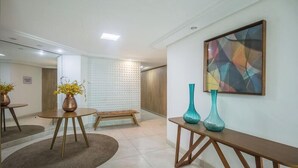 A modern hotel lobby with a round wooden table, a bench, and two vases on a console table.