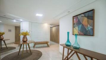 Um hall de hotel moderno com uma mesa redonda de madeira, um banco e dois vasos sobre uma mesinha.