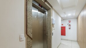 An elevator with a digital display, a fire extinguisher, and a red emergency door in a hallway.