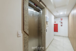 An elevator with a digital display, a fire extinguisher, and a red emergency door in a hallway.