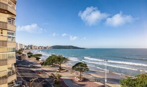 Un paisaje urbano costero con una playa, una carretera con coches y un edificio grande con balcones.