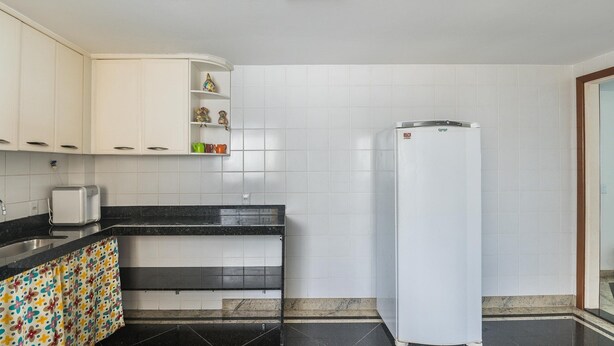 A kitchen with white cabinets, a black countertop, a white refrigerator, and a tiled backsplash.