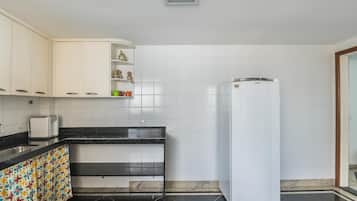 Cozinha com armários brancos, bancada preta, geladeira branca e painel de azulejos.