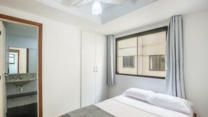 A bedroom with a bed, a window with curtains, a ceiling fan, and a bathroom with a sink and mirror.