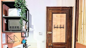 Une cuisine compacte avec un plan de travail en bois, une machine à café et un évier. On y trouve une porte en bois, un porte-manteau et une plante accrochée au mur.