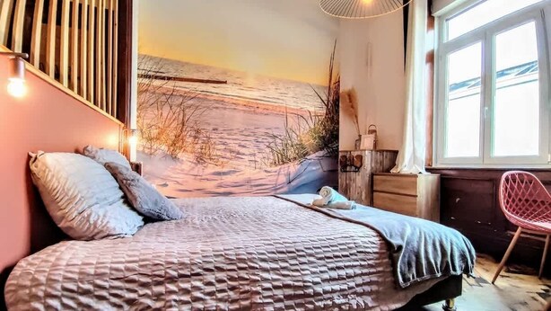 Une chambre à coucher avec un lit, une fenêtre, une chaise et une fresque murale.
