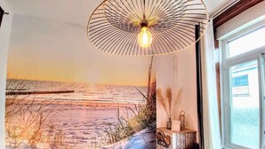 Une pièce décorée d’une fresque représentant une plage, avec un banc en bois, une table et un luminaire suspendu.