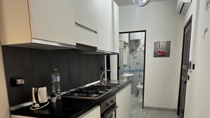 A modern kitchen with a gas stove, oven, and a water dispenser. There is a sink and a mirror above it. The kitchen has white cabinets and a black countertop. - Apartment° Fiumicino Rosy 3 (Isola Sacra)