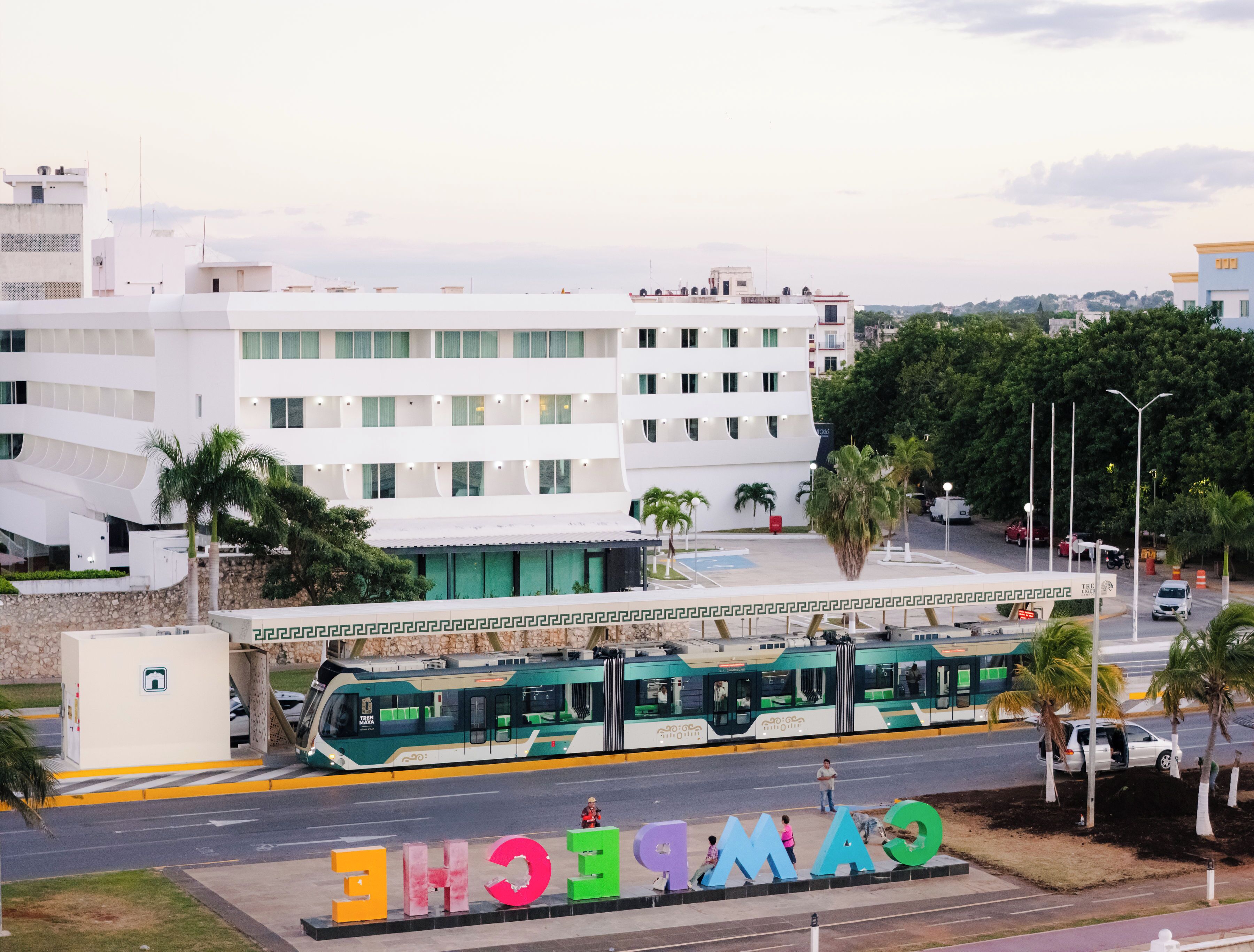 A modern building with a flat roof, a green bus, and palm trees.