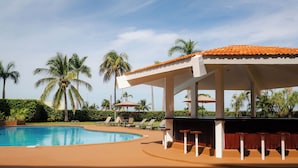 Piscina con sillones de descanso y una zona de estar cubierta.